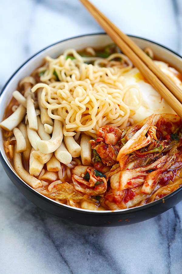 Easy and delicious homemade Korean ramen with kimchi, mushroom and poached egg in a bowl with a pair of chopsticks.