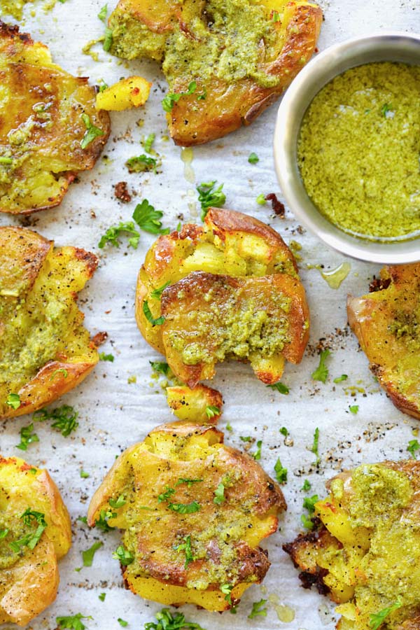 Baked smashed baby potatoes topped served with a side of garlic pesto dressing sauce.