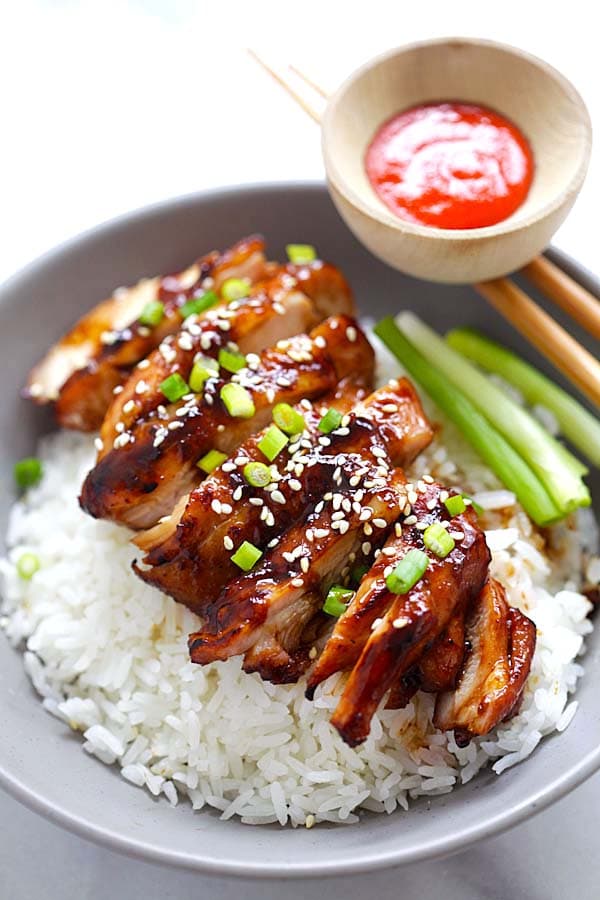 Easy healthy homemade soy-glazed chicken serve on top of steamed rice in a bowl with a pair of chopsticks and a side of red dipping sauce.