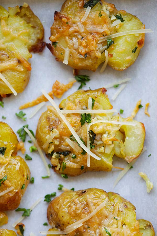 Close up Garlic Parmesan Smashed Potatoes, topped with chopped parsley, shredded Parmesan cheese and chopped garlic.