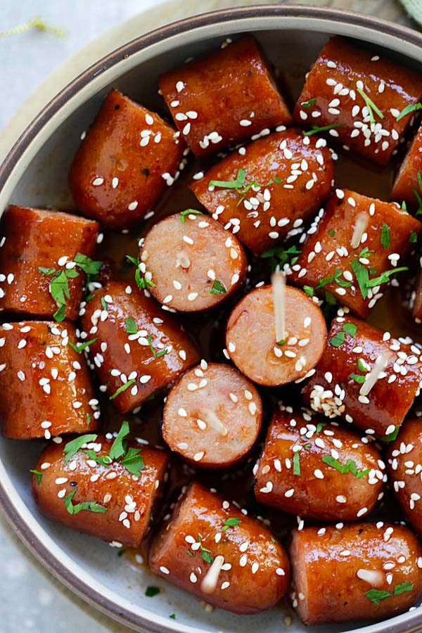 Honey Sriracha Sausage bites cut into small pieces, with a side of honey sriracha sauce, on a wooden chopping board.