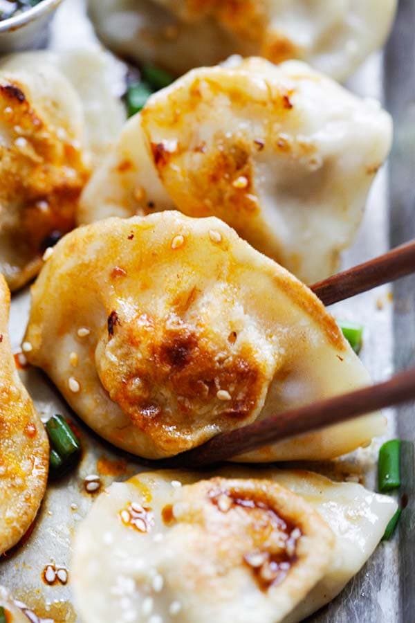 Homemade pan-fried Asian chicken dumplings picked up by chopsticks.