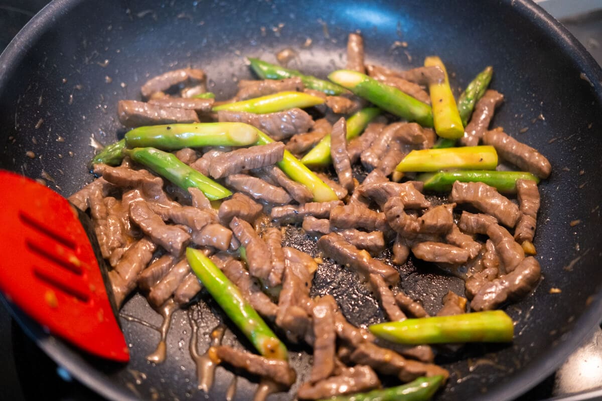 Stir fry the beef and asparagus in a wok. 