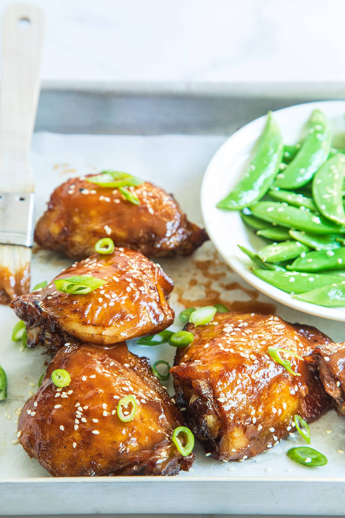 Healthy homemade Asian baked  chicken glazed with sweet honey soy sauce in a serving dish with a bowl of edamame on the side.