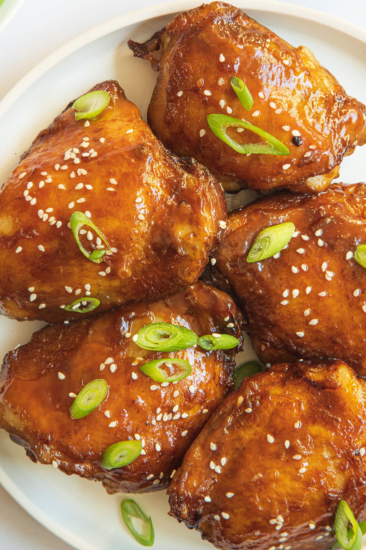 A close up shot of golden-brown glazed chicken thighs with scallion and white sesame sprinkled on top. 