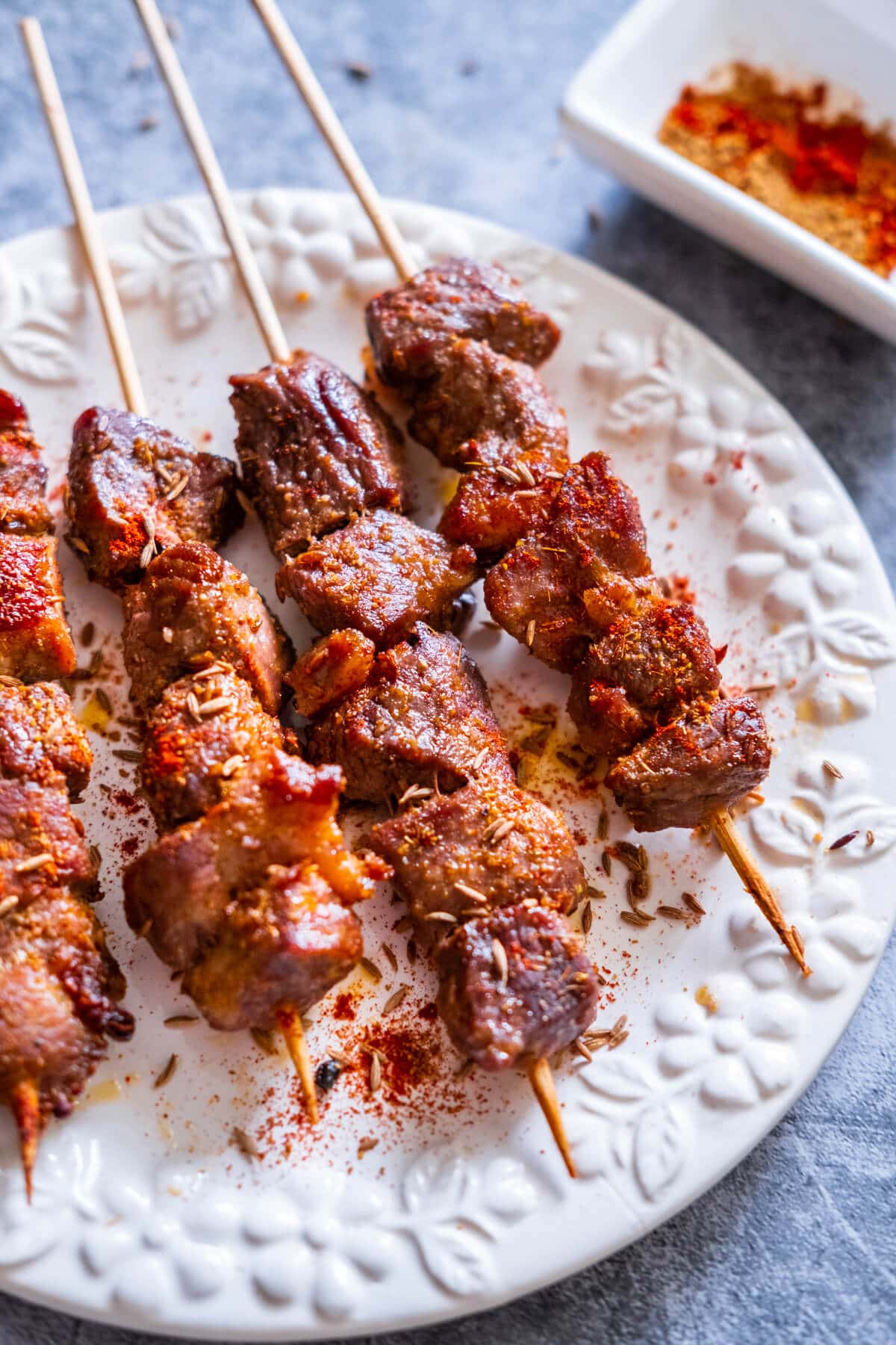 Lamb skewers served on a plate with chili powder aside. 