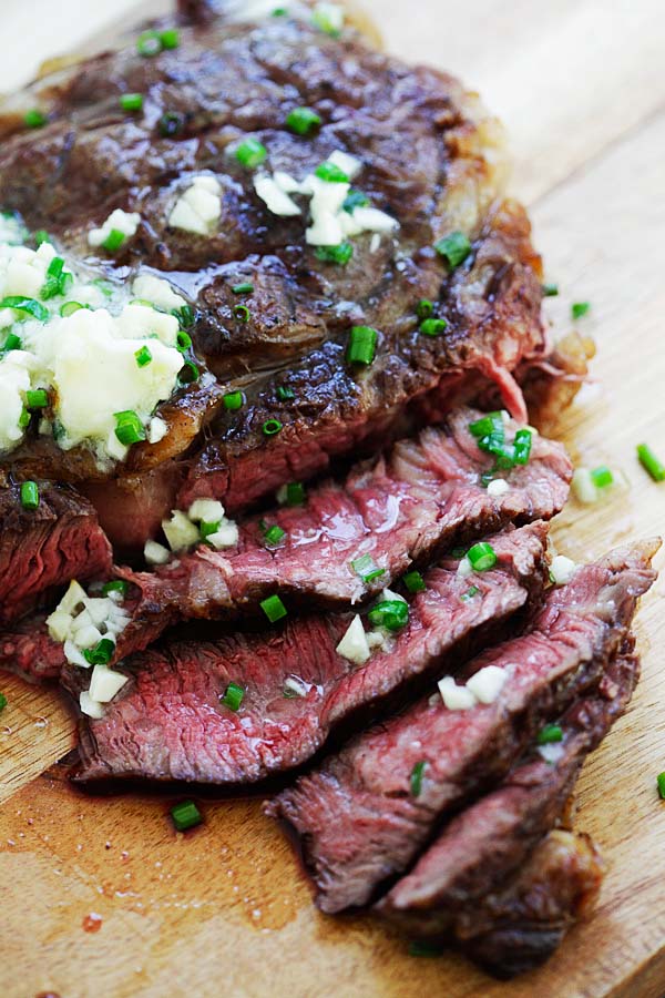 Homemade steak with garlic chive butter sliced and placed on wooden chopping board.