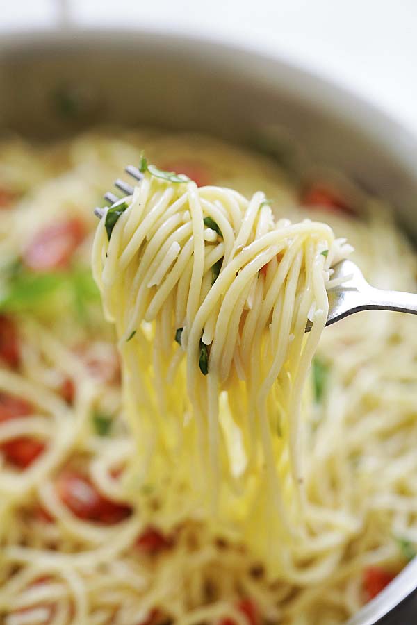 Zbliżenie makaronu spaghetti z sosem cytrynowym i bazylią nabraną na widelec.