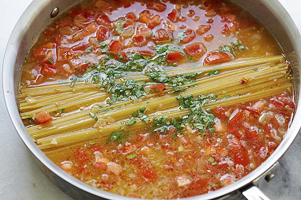 Spaghetti, tomatoes, chicken broth and herb in a pot for one pot pasta.