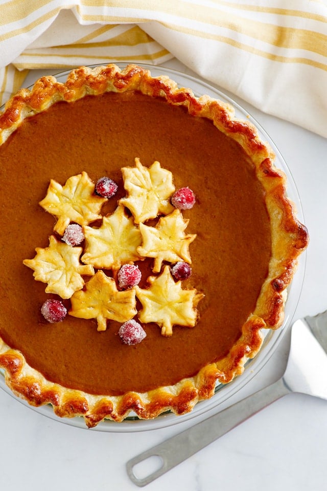 Pumpkin Pie in a glass pie plate, decorated with autumn leaves and candied cranberries.