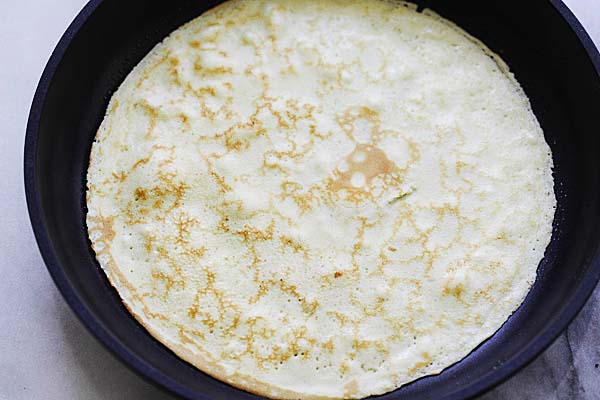 A crepe with brown spots on a non-stick pan.