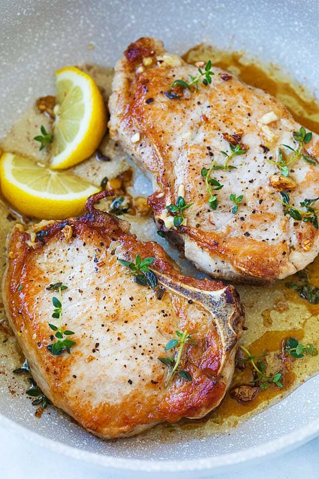 Garlic butter pork chops in a skillet with lemon wedges on the side.