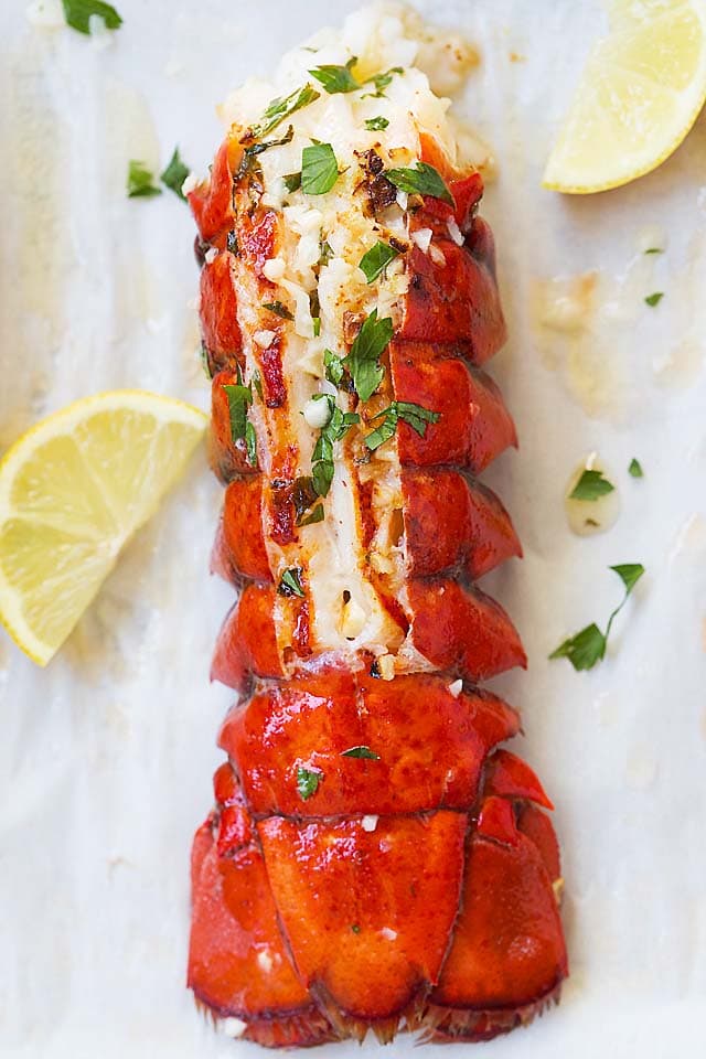 Oven baked lobster tails in garlic herb and lemon butter on baking sheet.