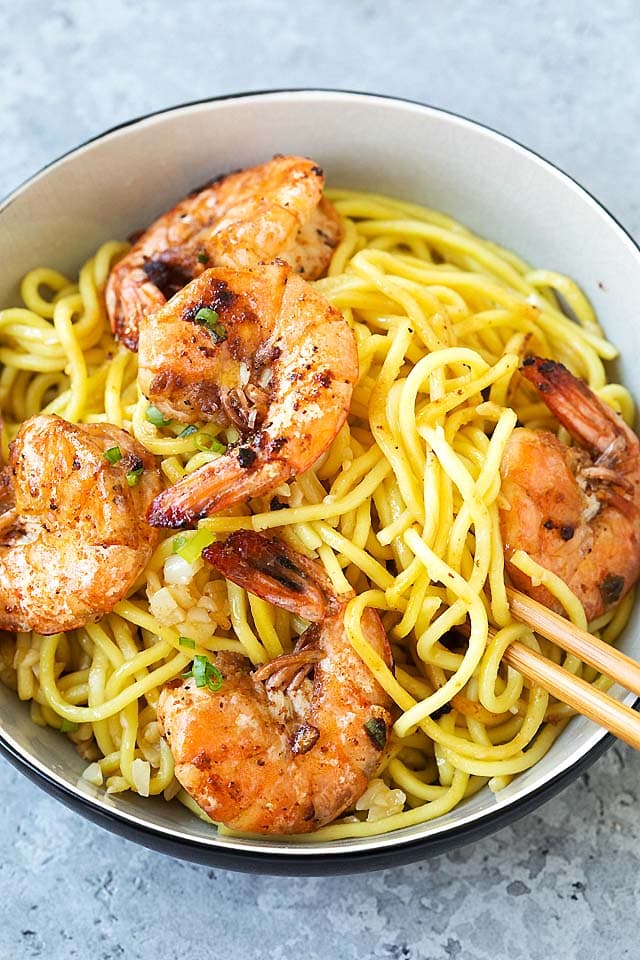 A pair of chopsticks picking up healthy homemade garlic noodles in a bowl.