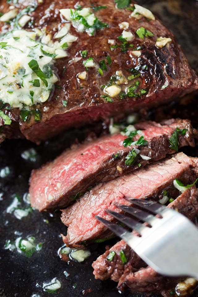 Medium rare top sirloin steak cooked in a skillet and served with garlic herb butter.