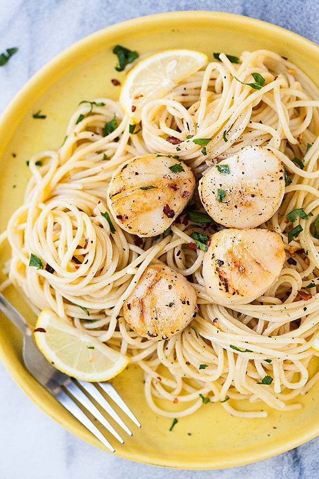 Close up photo of creamy spaghetti, topped with scallops on a yellow plate, with a fork. 