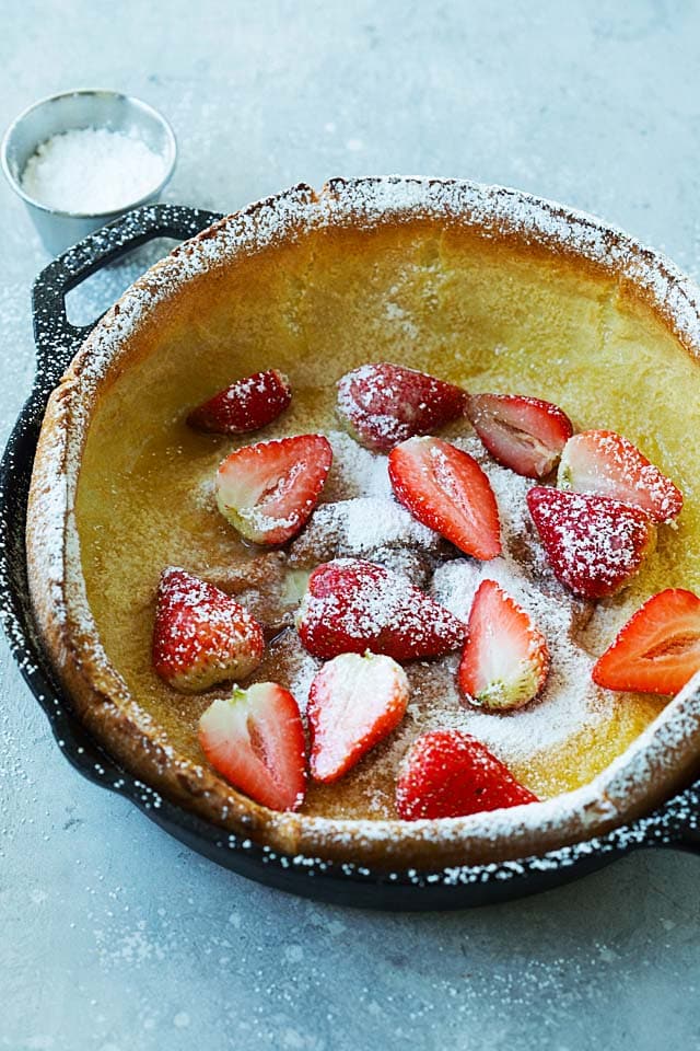 German pancake dusted with powdered sugar and sliced strawberry, ready to serve.