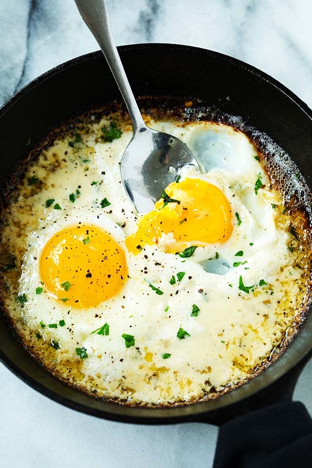 Easy sunny side up eggs cooked in a skillet, with heavy cream, Parmesan cheese and butter.
