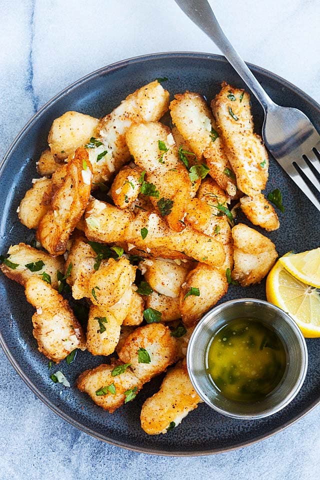 Crispy fish on a plate, with garlic butter sauce and lemon wedges.