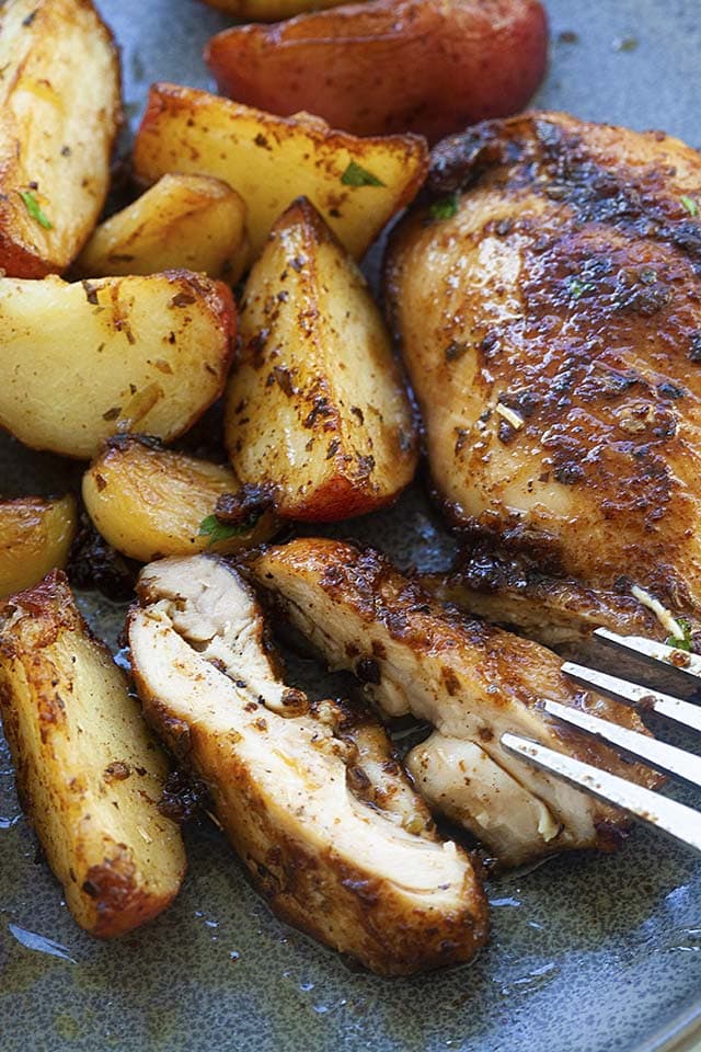 Chicken and potatoes sliced on a plate, ready to be served with a fork.