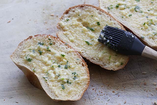 Brushing garlic butter spread on sliced bread.