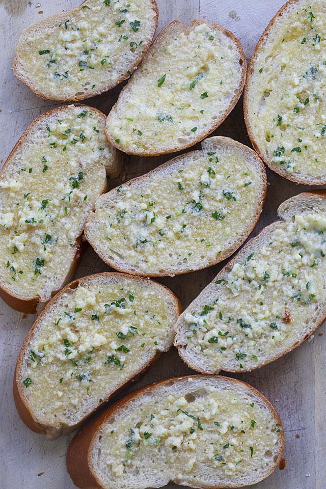 Sliced bread with buttery garlic bread spread on a tray, ready to be cooked on a skillet.