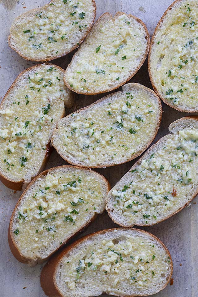  skiveskåret brød med smørret hvidløgsbrød spredt på en bakke, klar til at blive kogt på en stegepande.