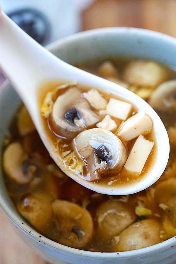 Hot and sour soup with mushrooms and eggs in stoneware bowl with spoon.