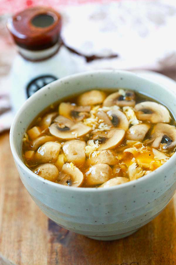 A bowl of hot sour soup with mushrooms, tofu and egg served with a side of additional vinegar. 