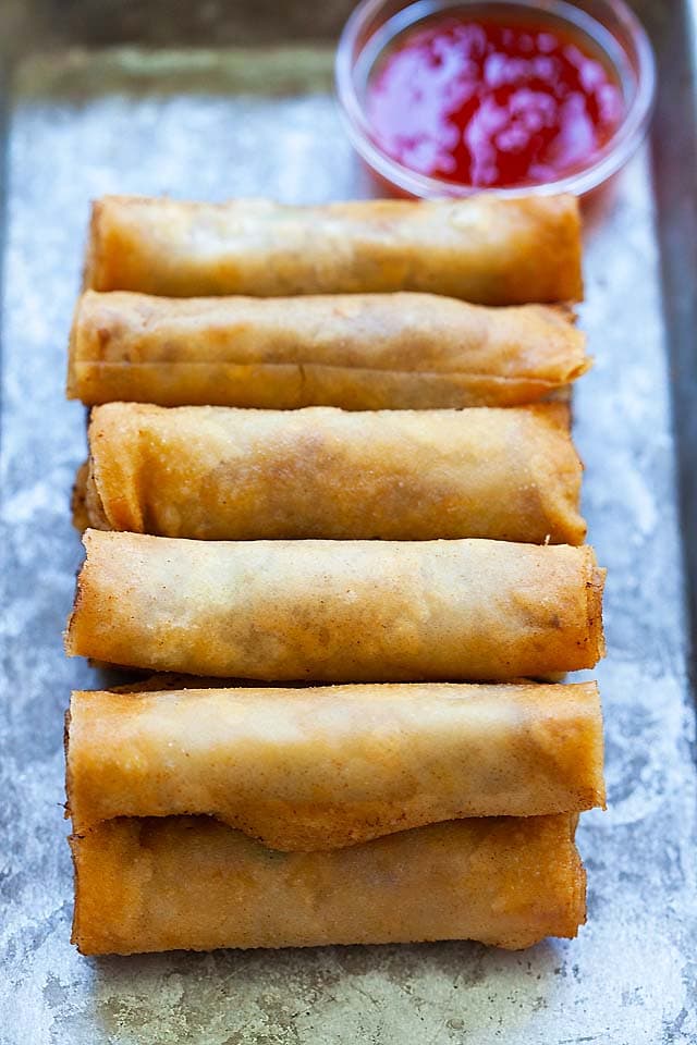 Open-ended crispy lumpia rolls on a serving platter with sweet and sour dipping sauce. 