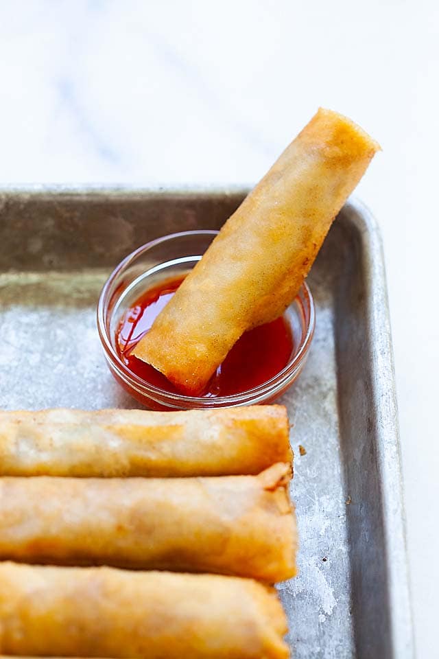 A lumpia dipped into a small bowl of lumpia sauce.