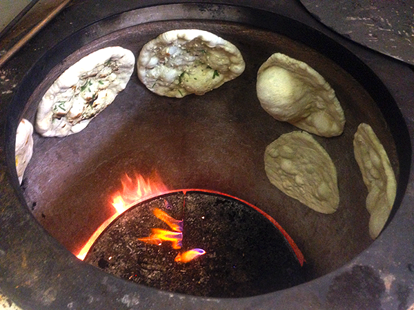 Making naan bread in a very hot Indian clay tandoor oven.