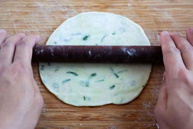 Rolling out a scallion pancake with a wooden rolling pin.