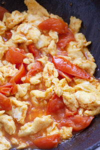 Tomato and eggs stir fried in a skillet.