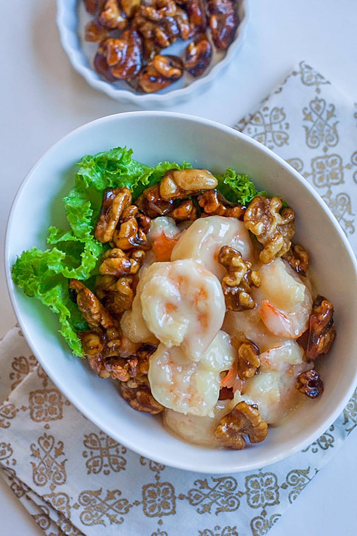 Honey walnut shrimp in a white bowl, with candied walnuts, ready to be served.