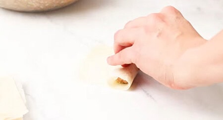 Rolling lumpia tightly and sealing with water.