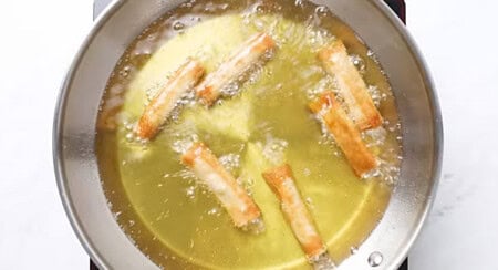 Deep frying lumpia rolls in a hot pan.