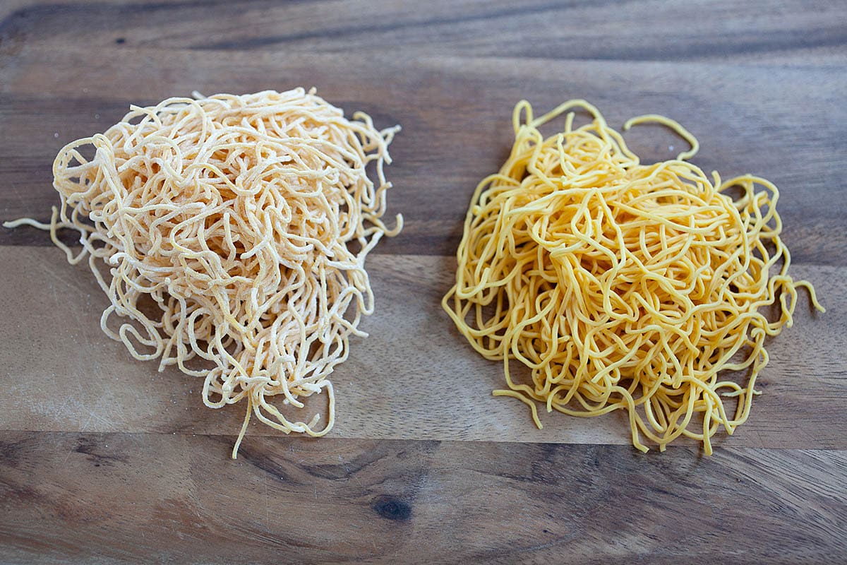 Two types of raw chow mein noodles on a chopping board. 