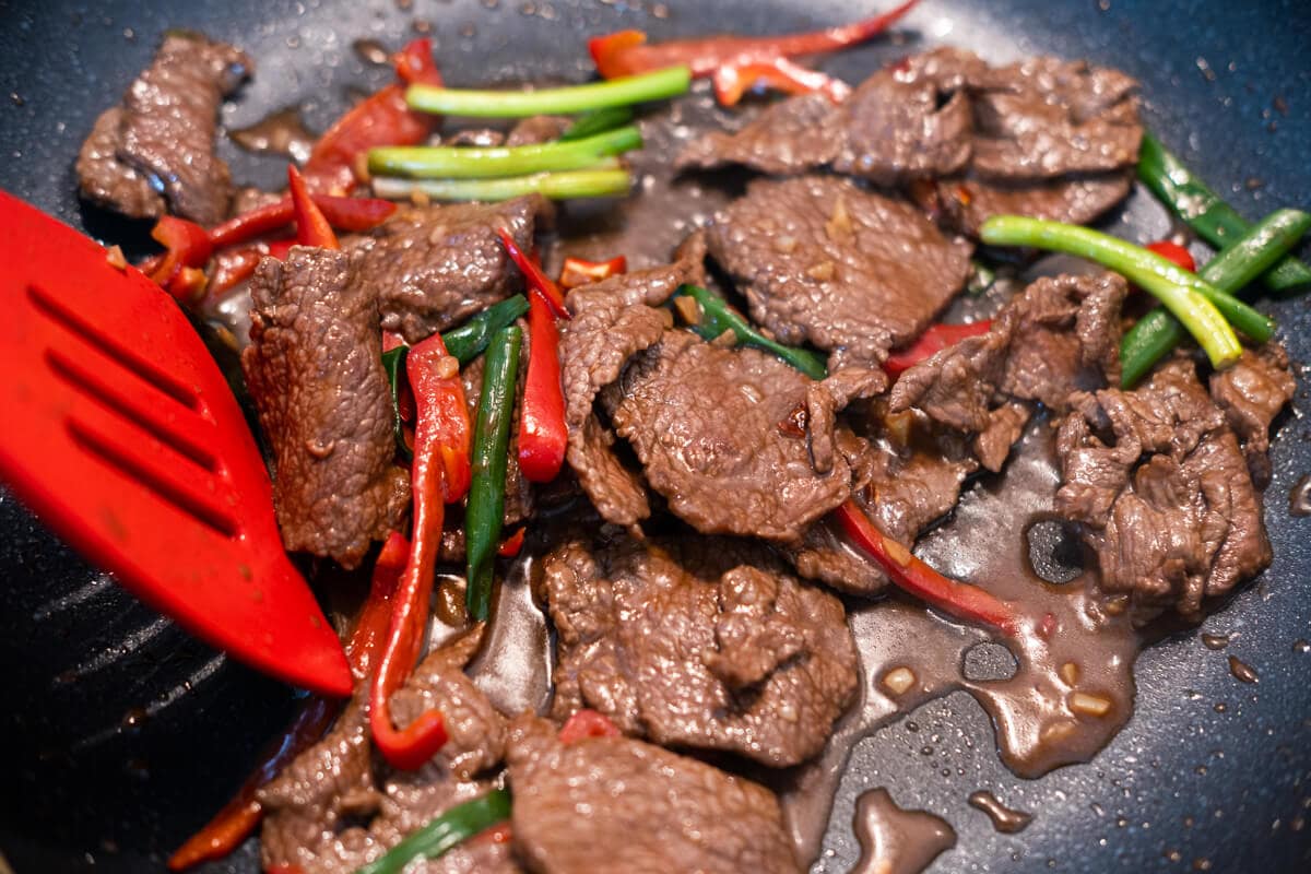 Stir-fry the beef slices with red bell pepper, chili flakes, and green onion in a brown sauce. 