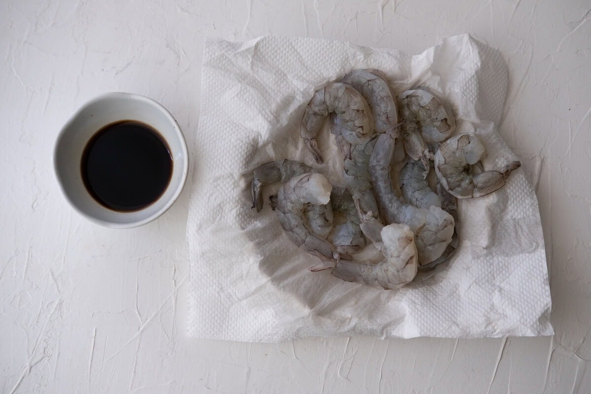 Shrimp being dried with a paper towel and bowl of dipping sauce made from soy sauce and vinegar. 