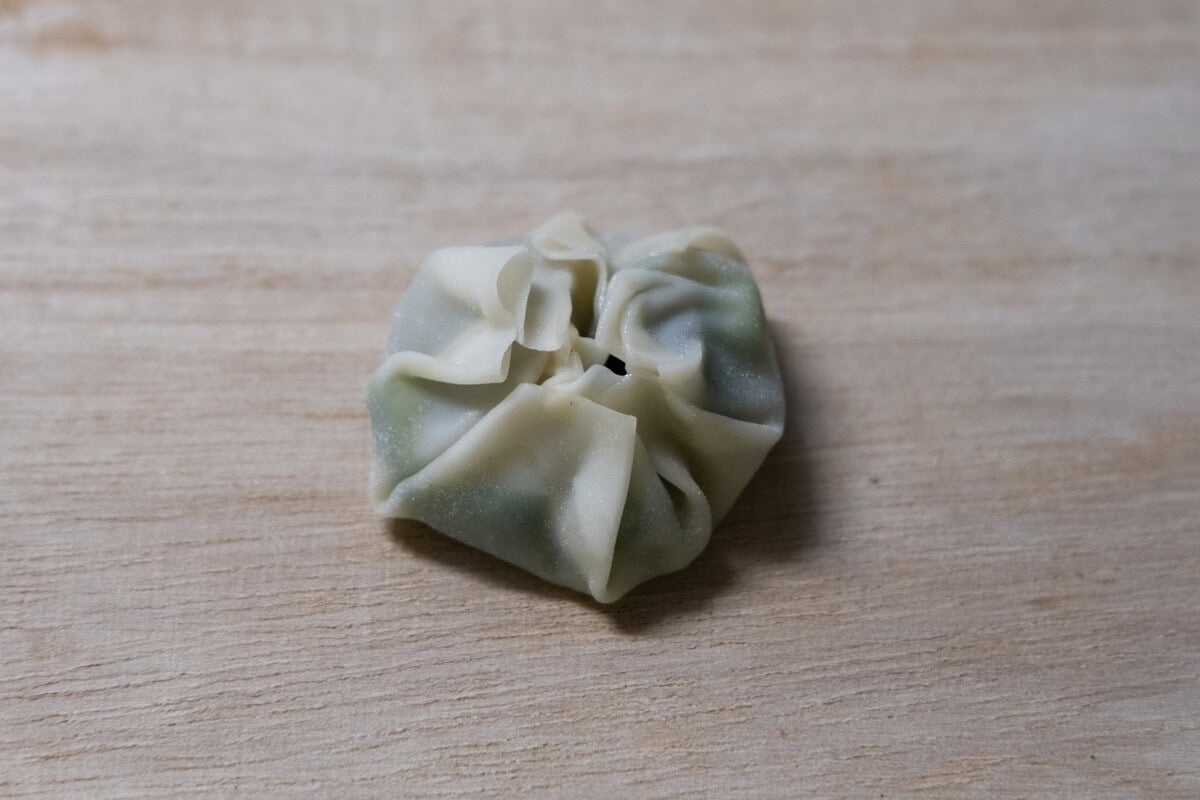 Wonton skin with shrimp and chive filling is sealed and made into a round shape. 

