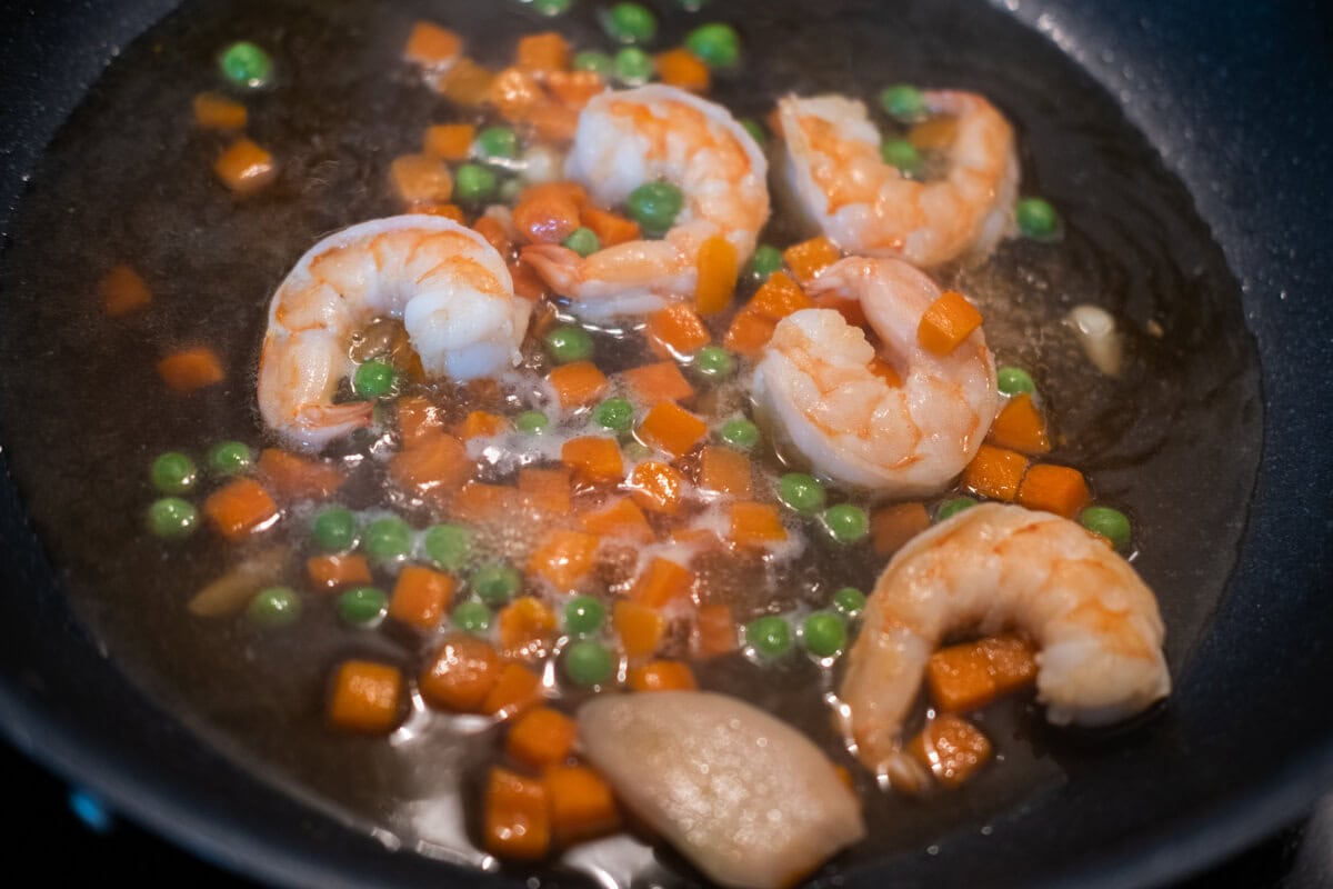 Adding frozen vegetables to the pan with shrimp. 