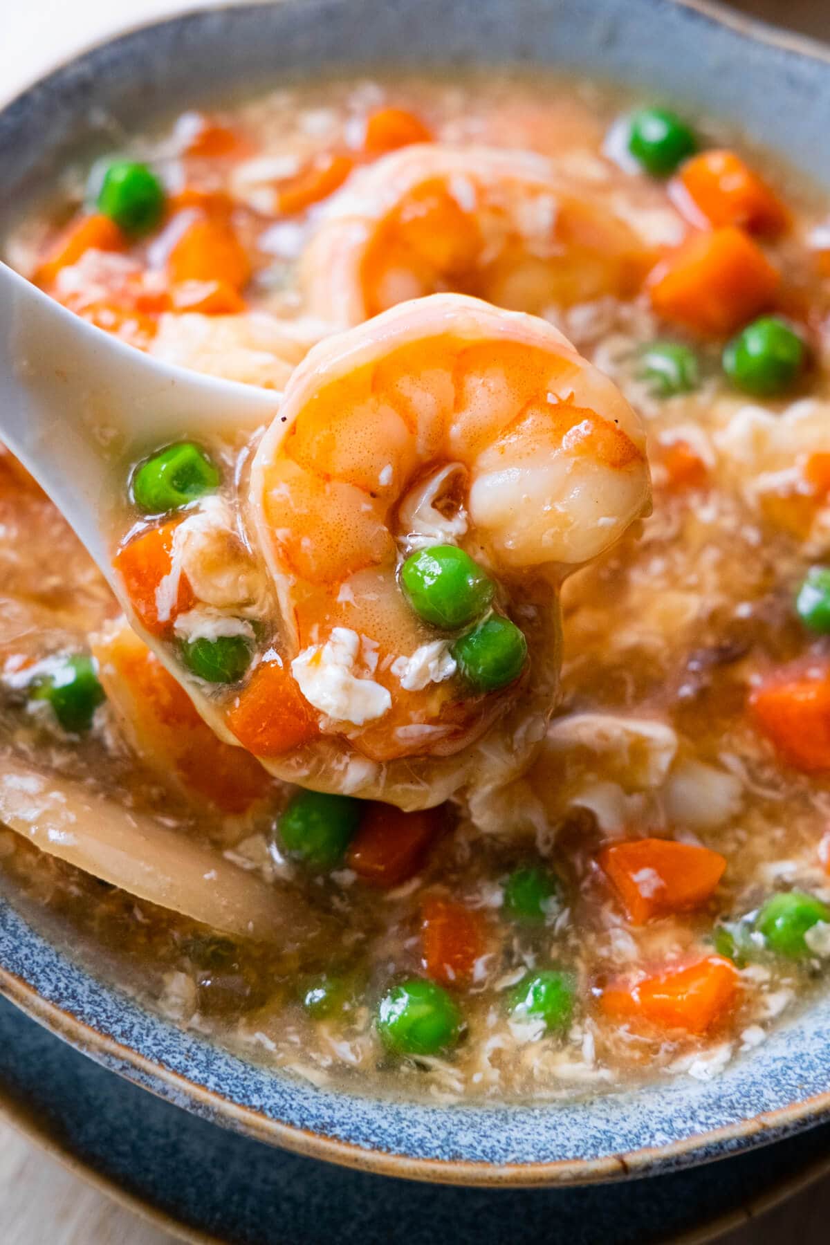 Shrimp with peas and carrots with lobster sauce on a spoon. 