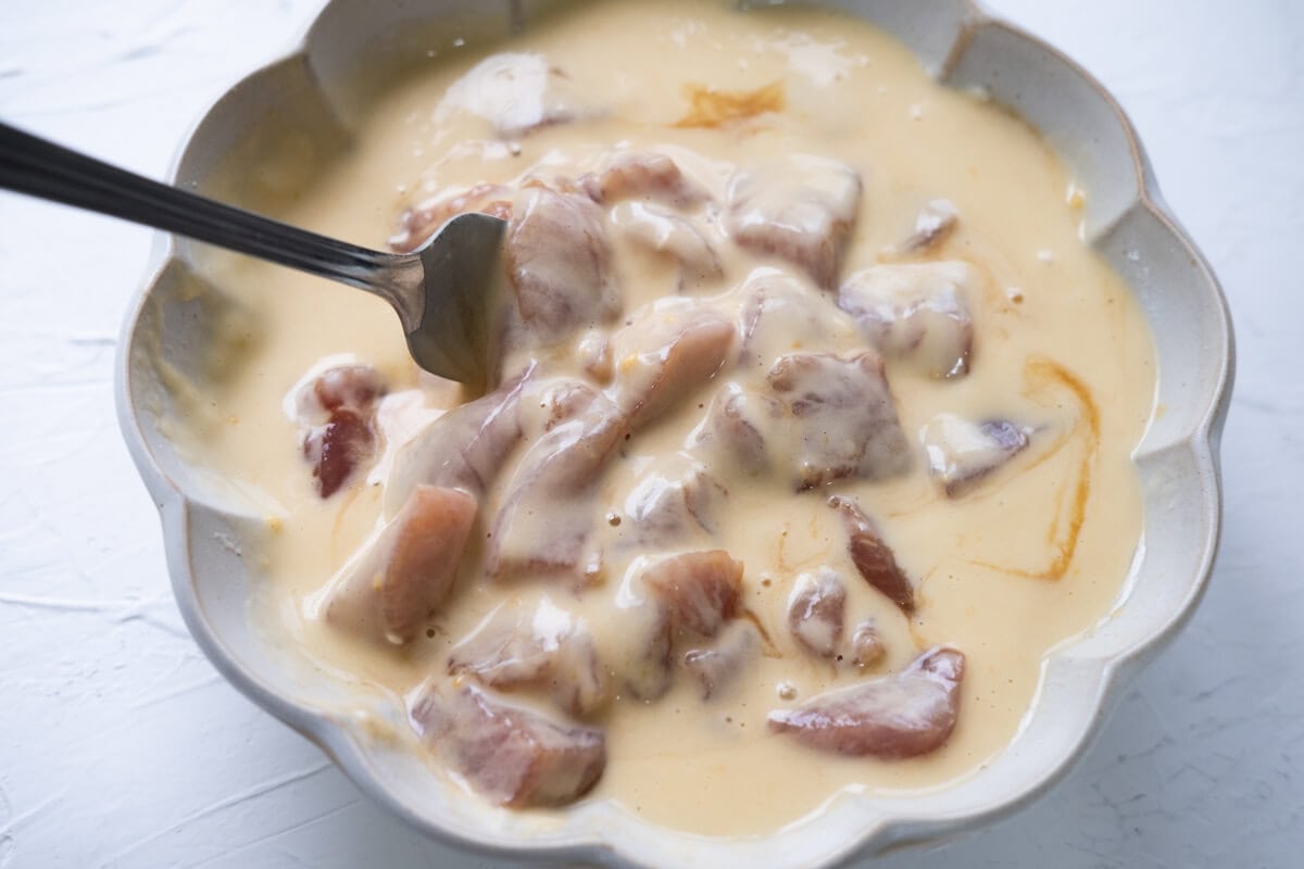 Coating marinated pork cubes with frying batter in a bowl. 