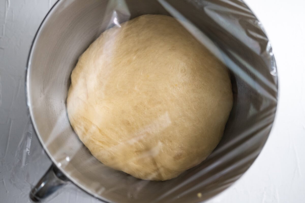 French brioche bread dough proofing in a bowl covered with plastic wrap. 