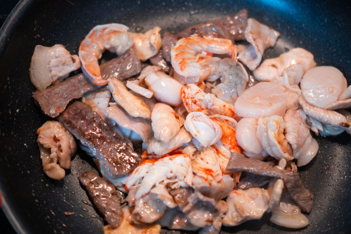 Stir-fry the pork, chicken, beef, scallop, shrimp and crab meat in a frying pan with the sauce. 