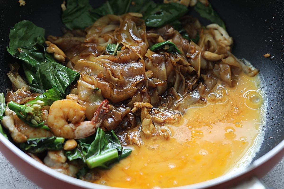 Adding beaten eggs to pad see ew noodles in a skillet. 