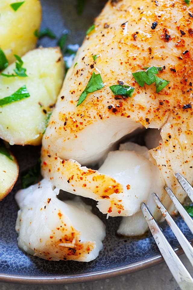 A fork poking through baked cod fillet, revealing flaky white meat. 