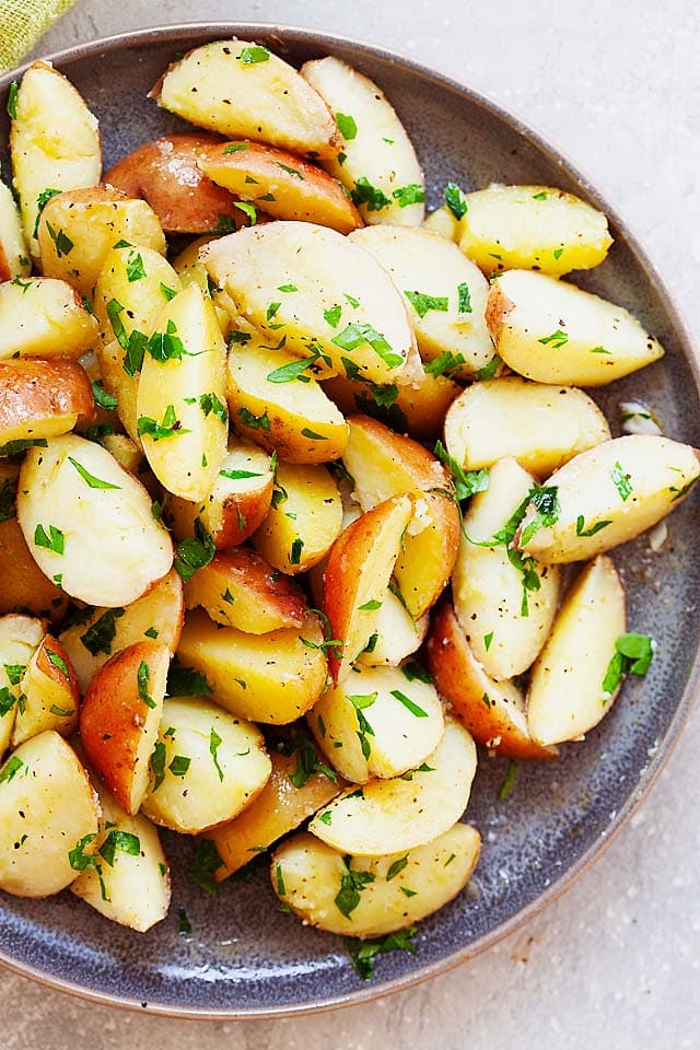 Pommes de terre rouges bouillies coupées en quartiers avec du beurre persillé, prêtes à servir.