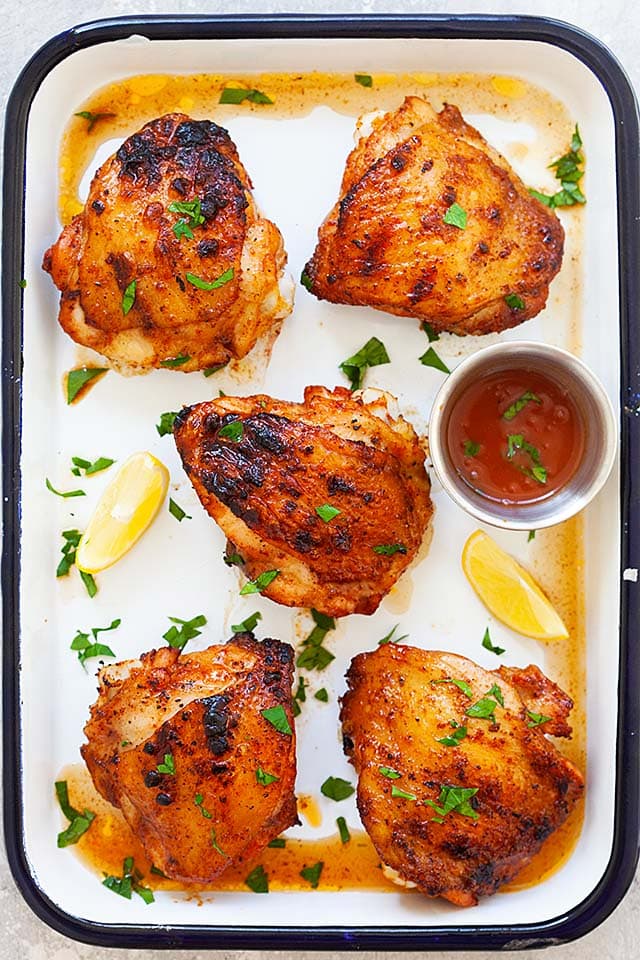 Grilled chicken thighs on a white serving tray, ready to serve.